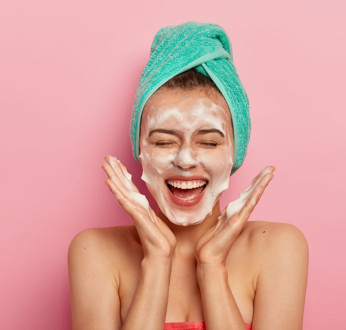 happy-joyous-young-girl-spreads-palms-face-washes-face-with-soap-has-fun-bathroom-pampers-skin-wears-wrapped-towel-head-expresses-positive-emotions